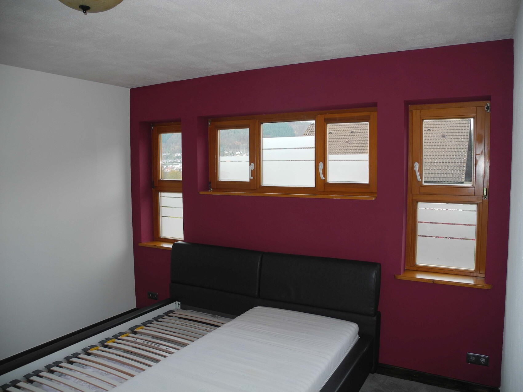 Schlafzimmer mit magenta Wand, Holzfensterrahmen und schwarzem Bettgestell