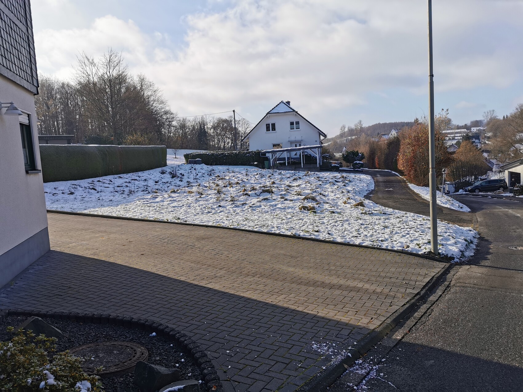 Winterliche Außenaufnahme eines Hauses mit verschneitem Vorgarten, Zufahrt und Straßenzugang.