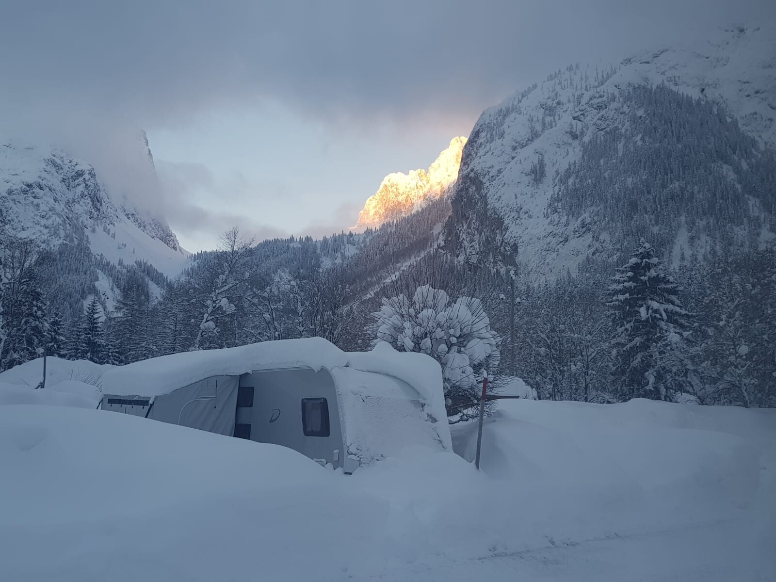 Verschneite Berglandschaft mit einem Camper, verschneite Bäume und Sonnenlicht auf dem Gipfel.