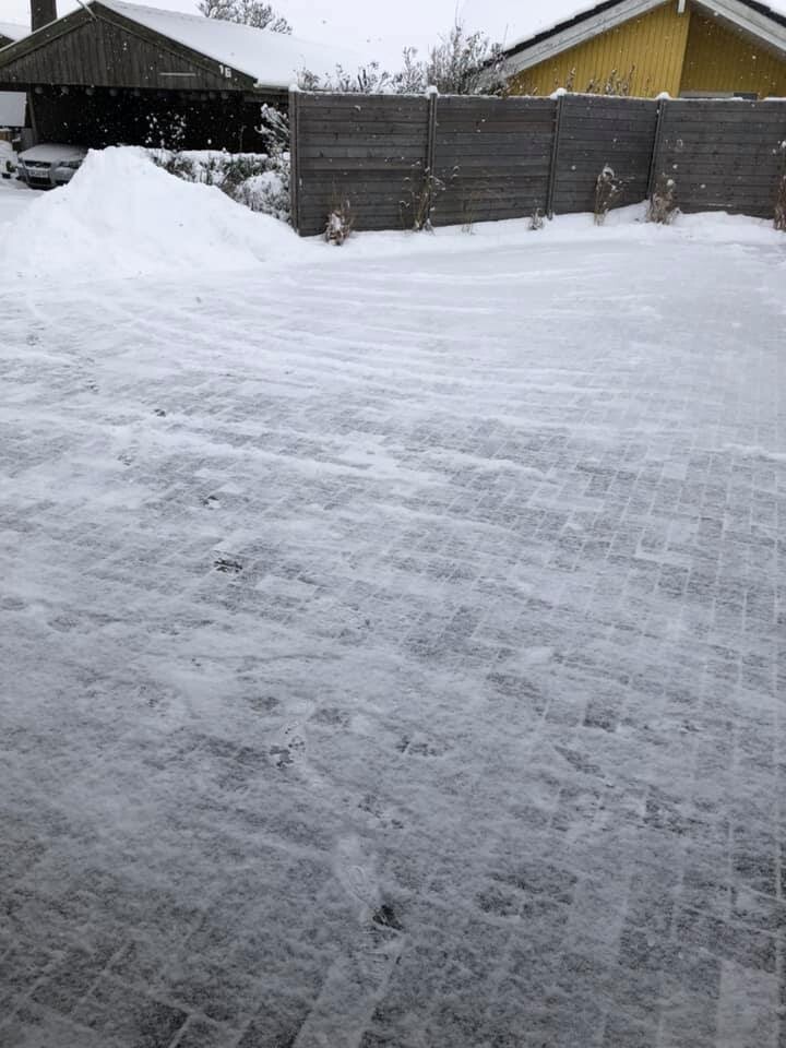Schnee bedeckter Hof mit Holzzaun, Garage links, gelbes Haus rechts, leichter Schneefall.