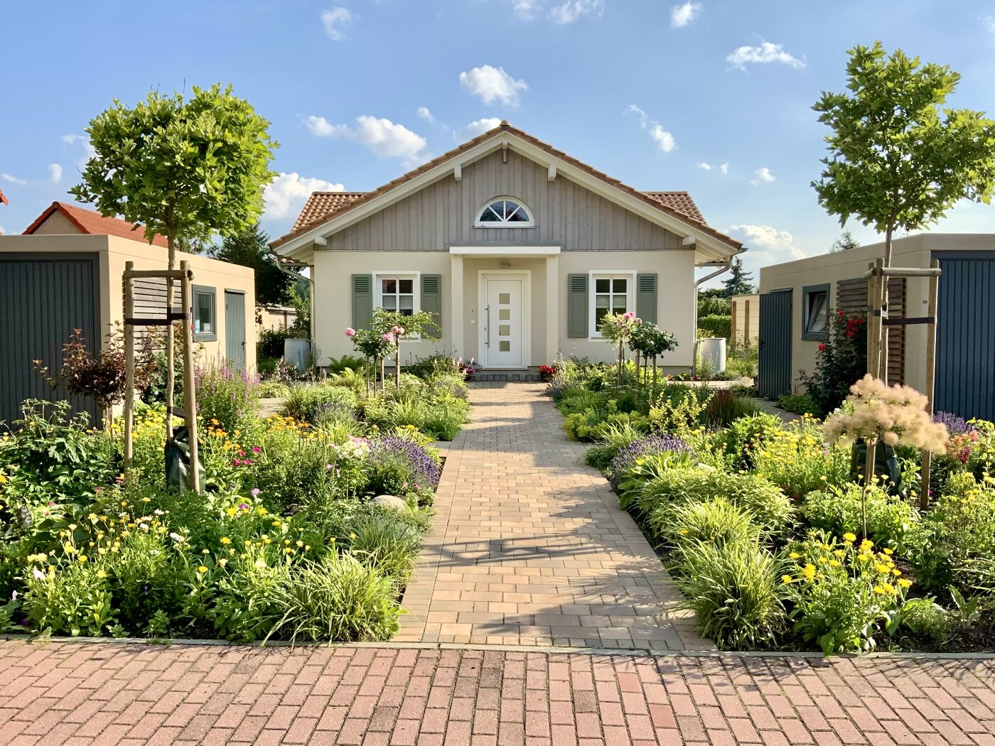 Helles Einfamilienhaus mit farbenfrohem Blumengarten und gepflastertem Weg zum Eingang.