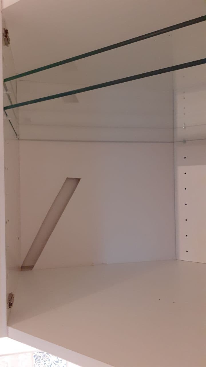 Offener weißer Schrank mit zwei dunklen Stangen; diagonales Holzbrett steht drin.