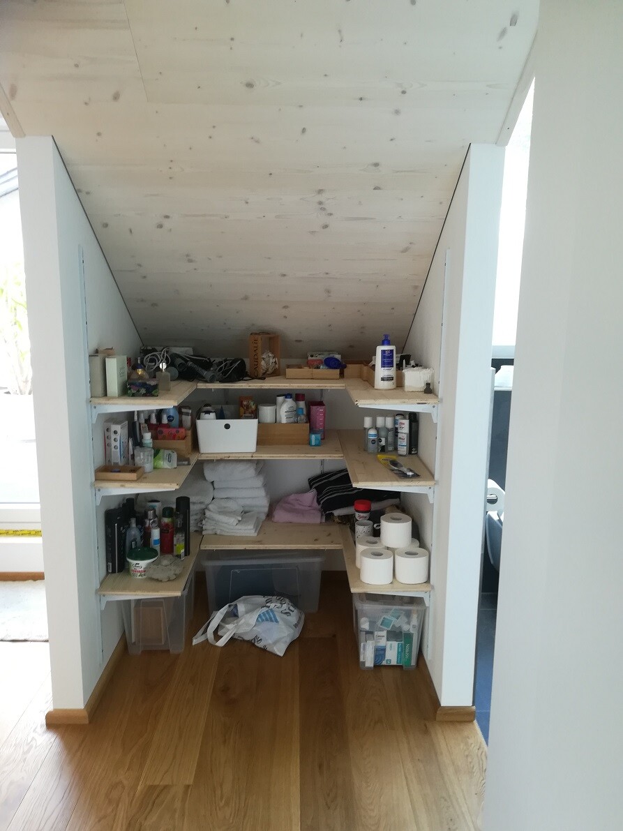Kompakter Abstellraum unter der Dachschräge mit Holzregalen voller Alltagsartikel und Toilettenpapier