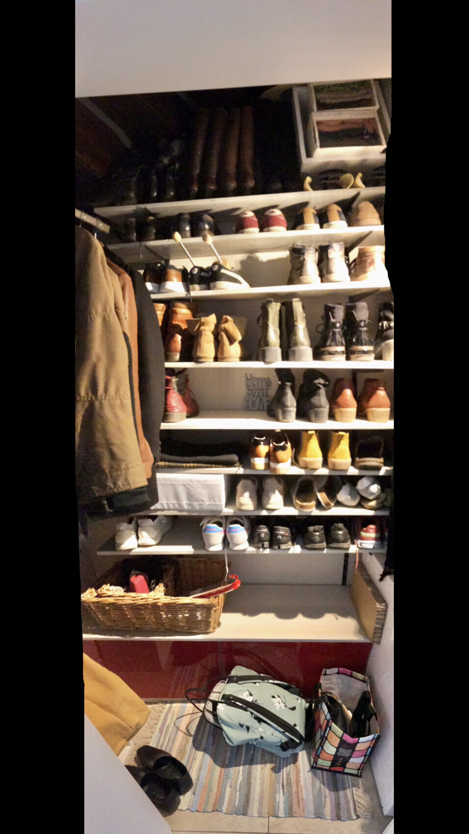 Offenes Schuhregal in einer begehbaren Garderobe mit Schuhen, Jacken und Taschen.