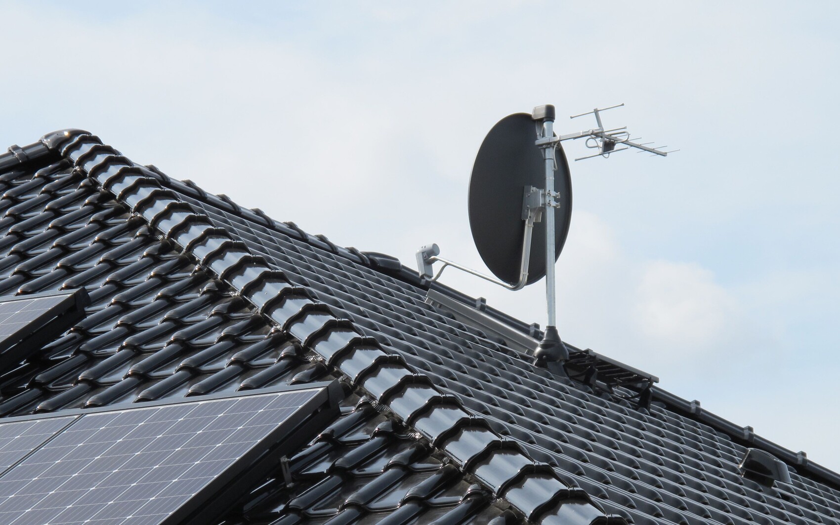 Dach mit schwarzen Tondachziegeln, Solarpaneele und Satellitenschüssel sowie Antenne