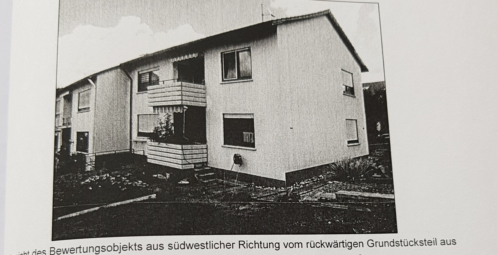 Zweistöckiges Mehrfamilienhaus mit Balkon, weiße Fassade, Gartenweg davor.