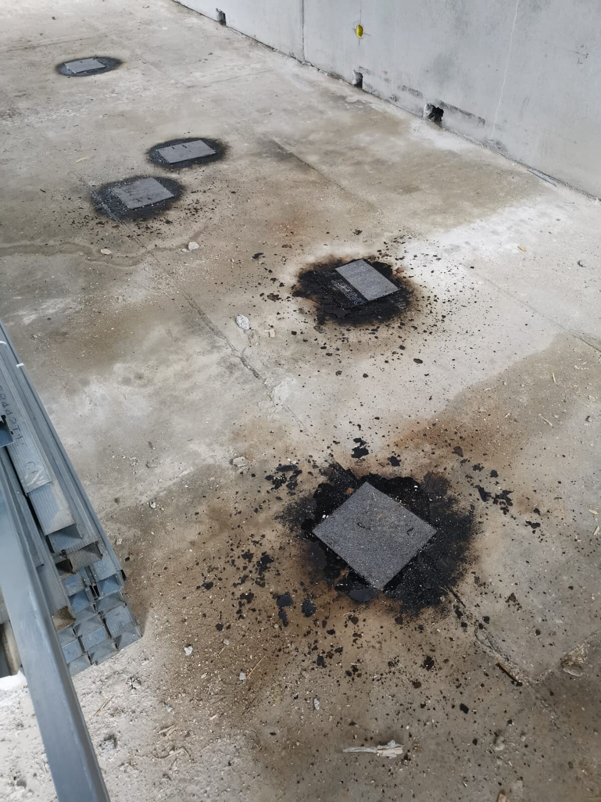 Baustelle: verbrannte, schwarze Flecken um quadratische Platten auf rohem Betonboden.