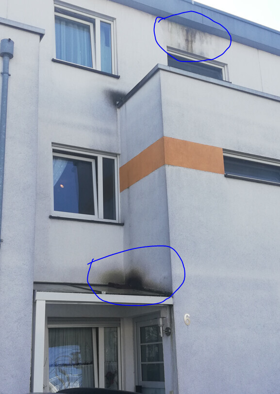 Außenfassade eines Gebäudes mit Rußflecken unter Fenstern und am Eingang.