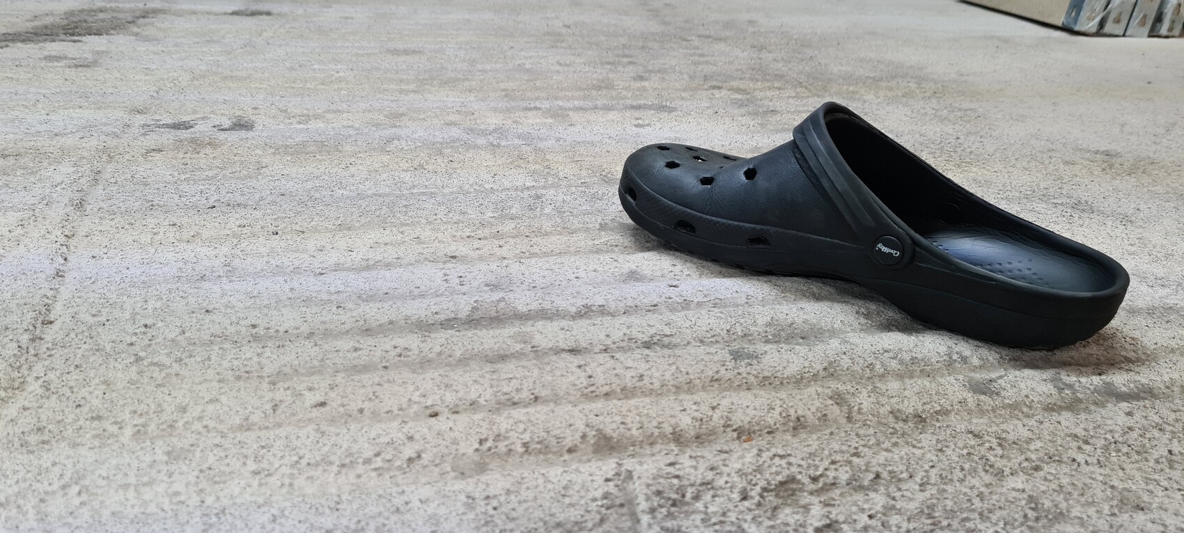 Ein einzelner schwarzer Crocs-Schuh liegt flach auf rauem Betonboden.