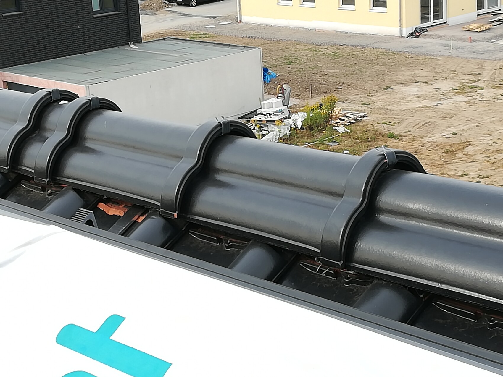 Dunkles Ziegeldach auf einer Baustelle, Bauplatz und gelbes Gebäude im Hintergrund