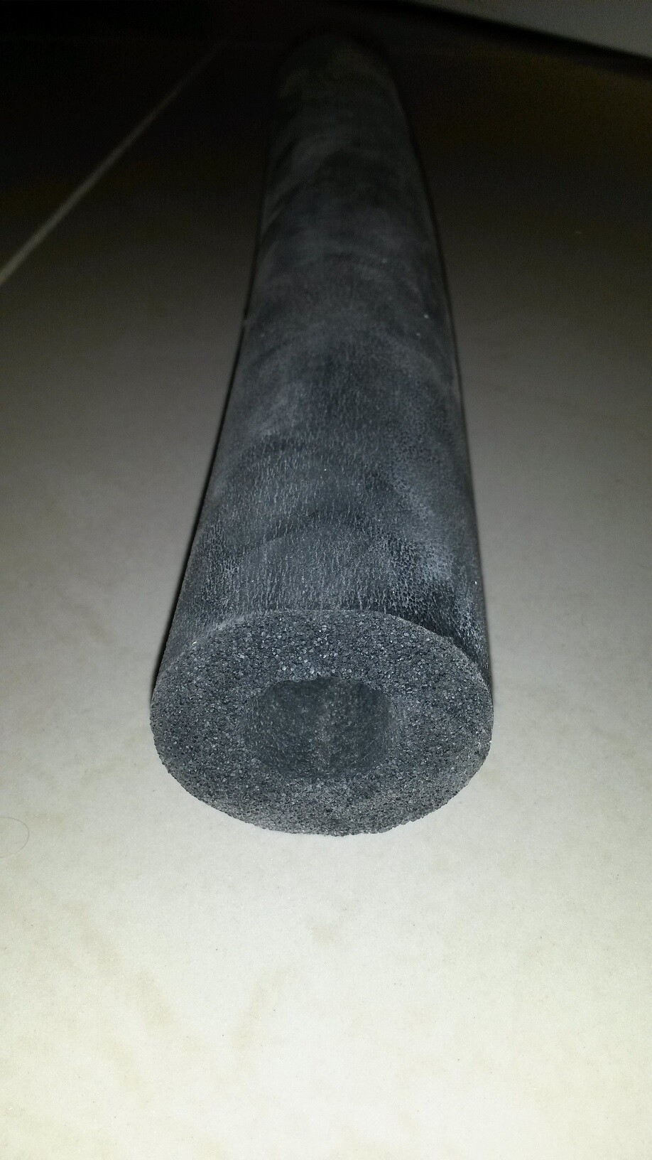 Schwarzer Schaumstoff-Zylinder liegt horizontal auf hellem Boden; Nahaufnahme, staubig.