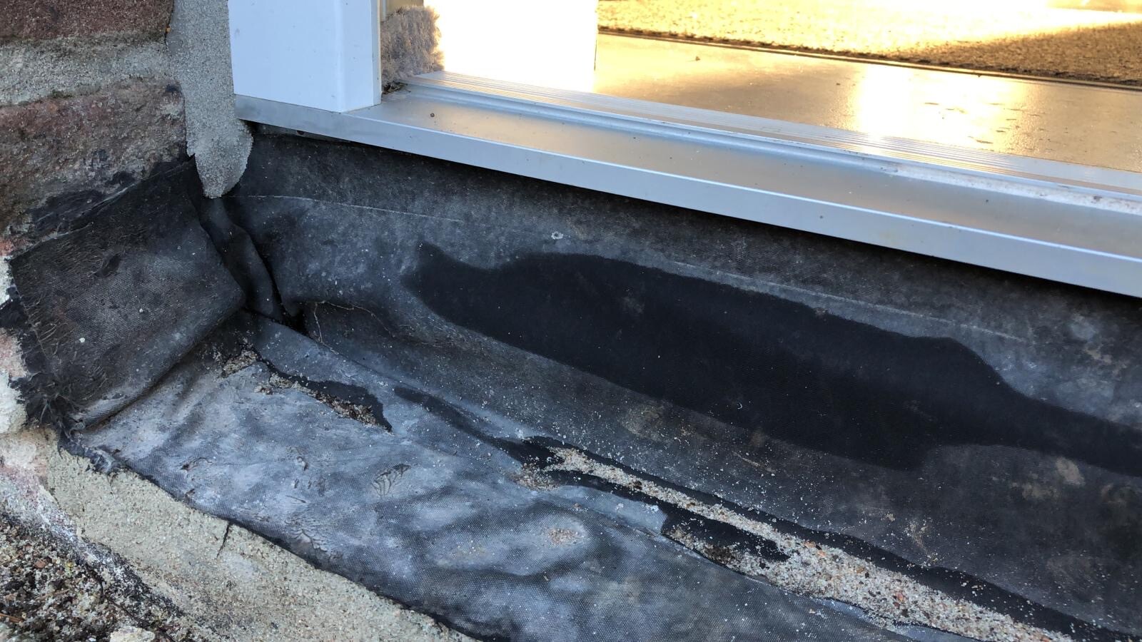 Fundamentbereich mit schwarzer Dichtungsbahn und Kies unter einer Fensteröffnung am Gebäude