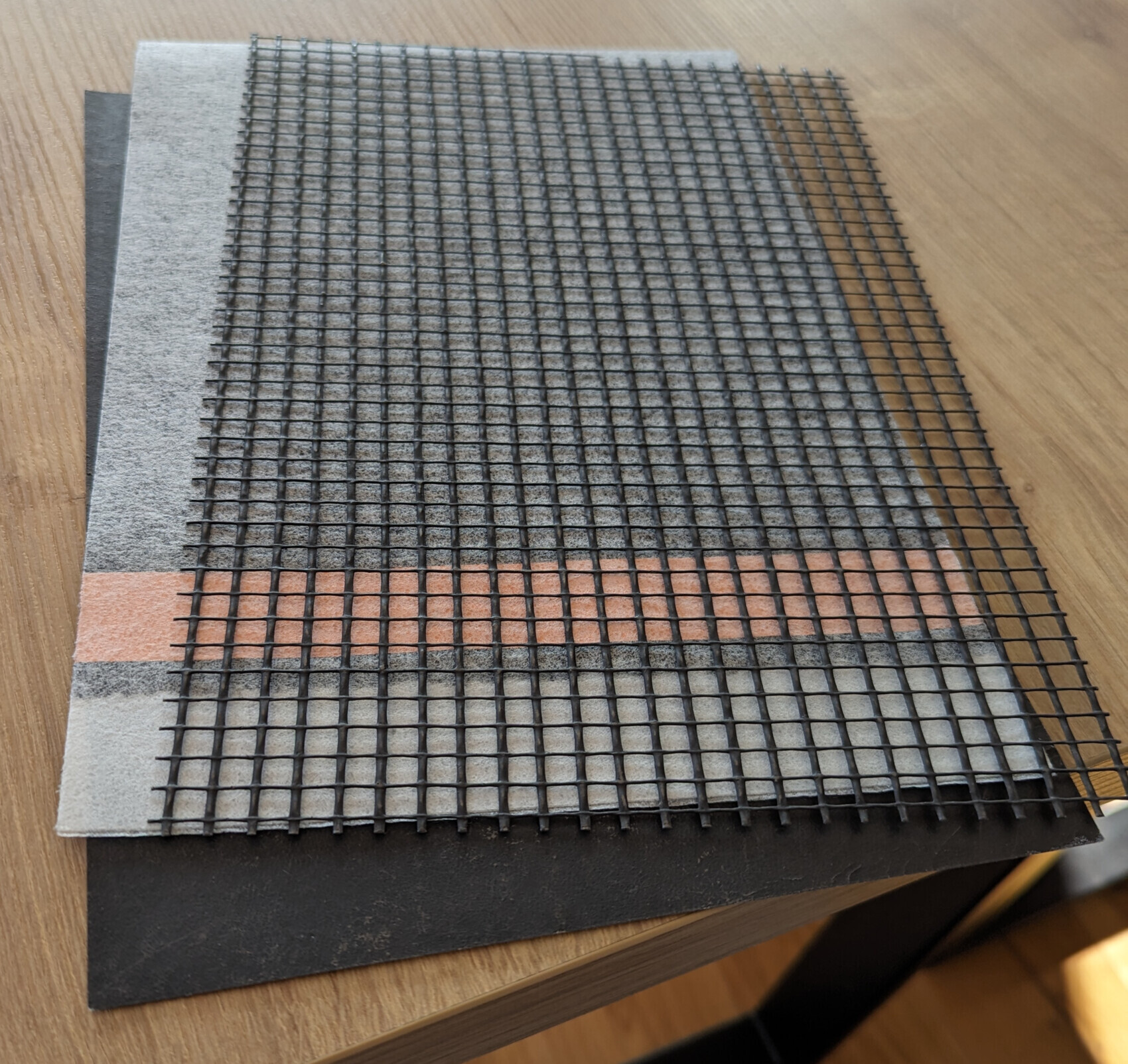Schwarzes Gitternetz liegt auf mehrlagigem Untergrund mit grauer Textur und rotem Streifen.