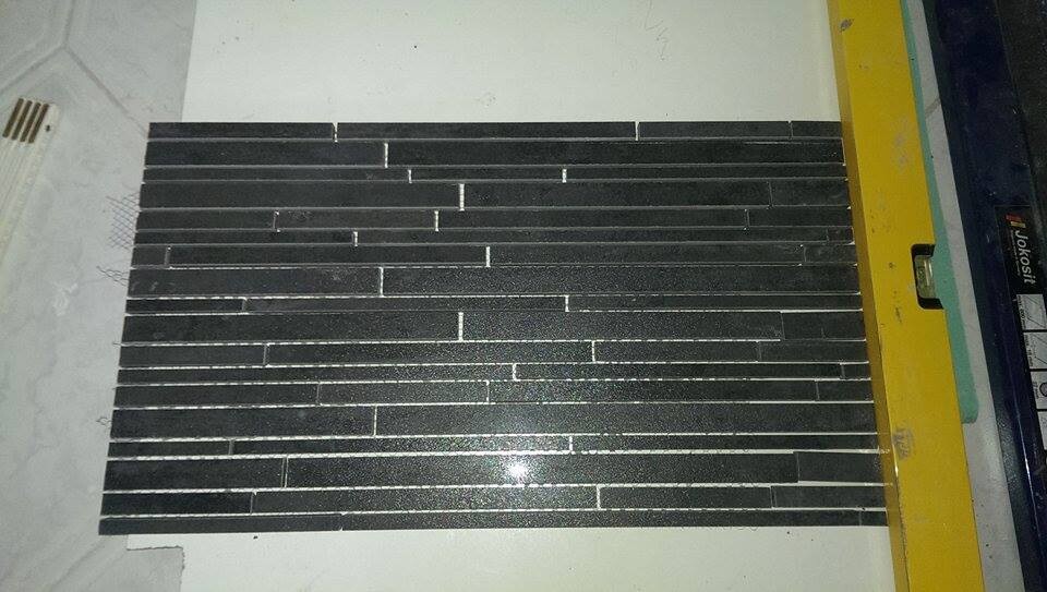 Schwarze rechteckige Glasmosaikfliesen liegen als Bodenbelag auf einer Baustelle
