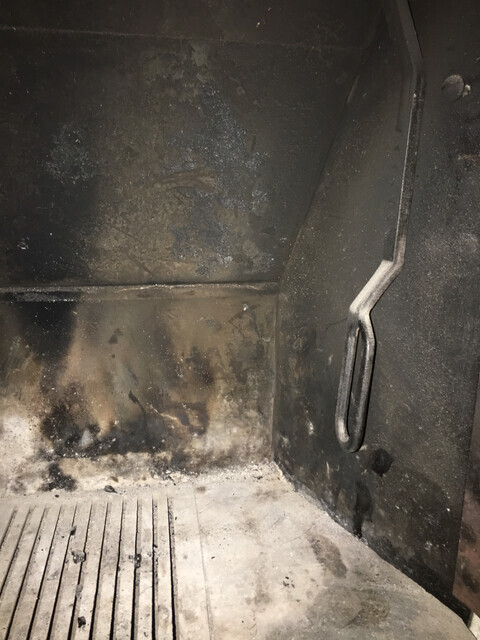 Inneres eines verrauchten Grills mit Asche, Ruß und einem Metallgriff an der Seite