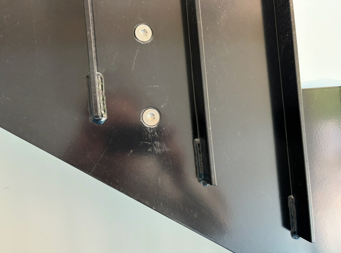 Nahaufnahme eines schwarzen Metallbeschlags mit Schrauben und Führungsleisten.