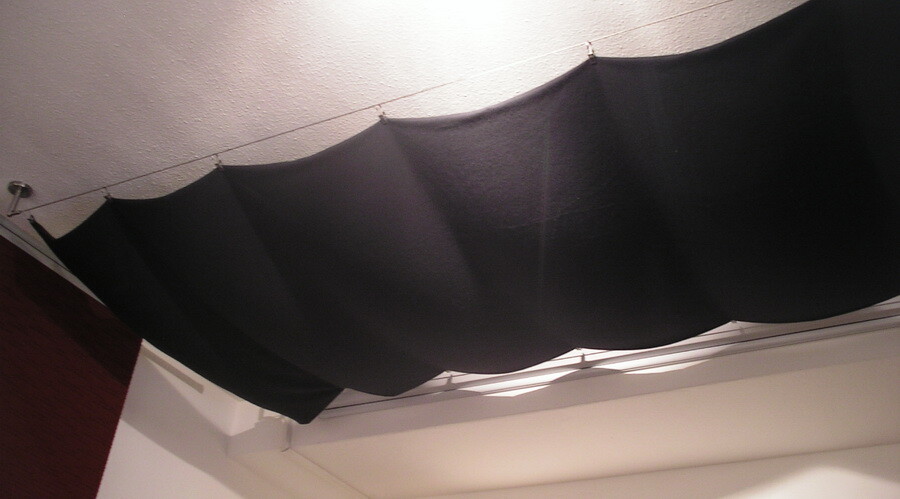 Schwarze Stoffbespannung hängt als Deckenverkleidung von der Decke in einem Innenraum.
