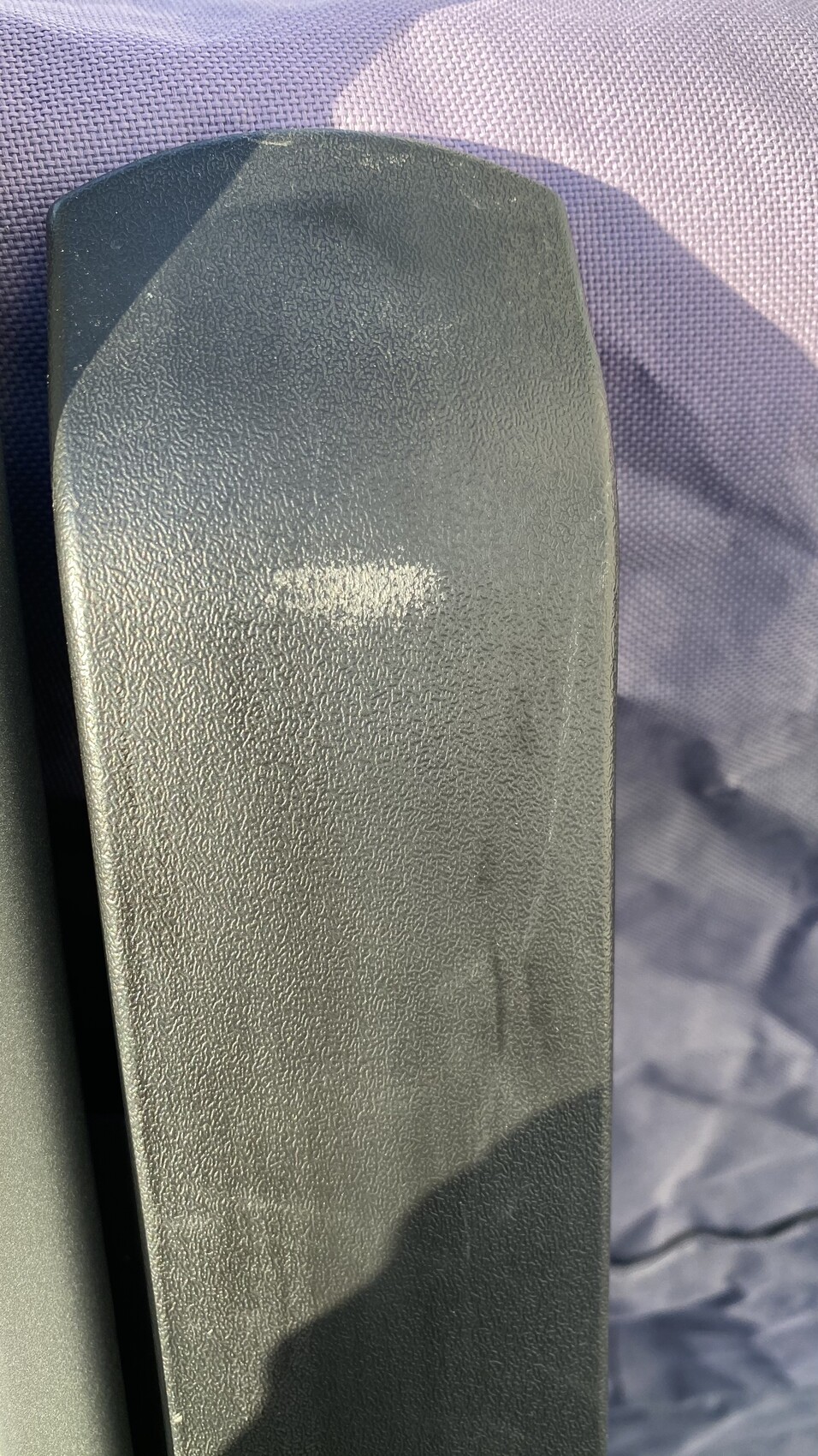 Nahaufnahme einer schwarzen Armlehne aus Kunststoff auf violettem Stoffbezug, texturiert.