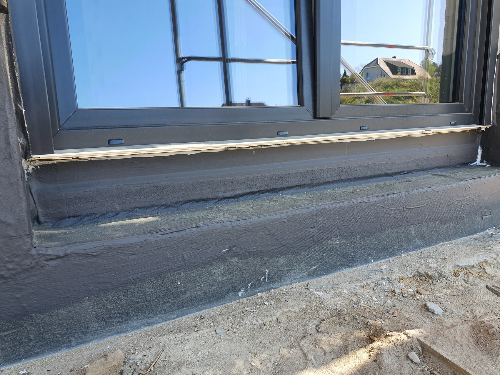 Neu installiertes Fenster mit dunkelgrauem Rahmen, Abdichtung am Sockel, Baugerüst im Hintergrund.