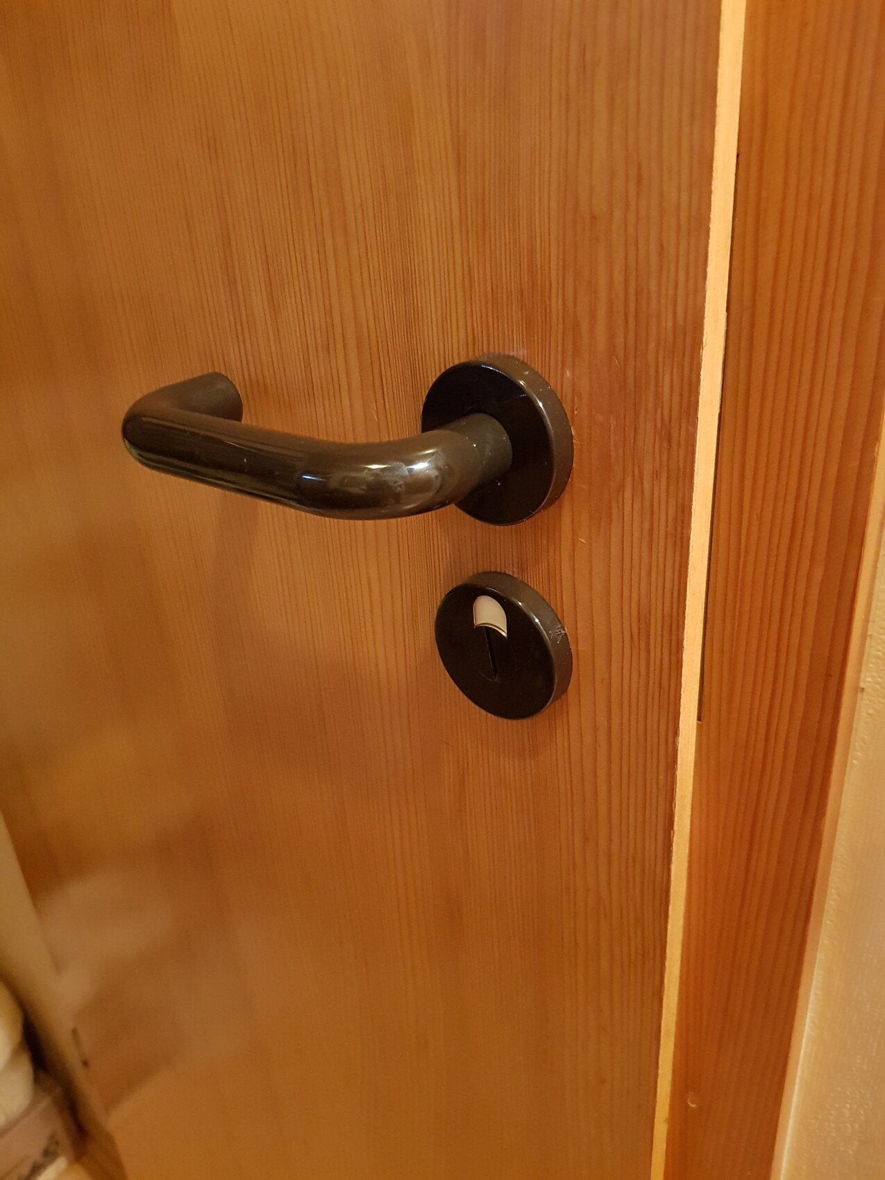 Holztür mit schwarzem Metall-Türgriff und runder Schlossrosette mit Schlüsselöffnung.