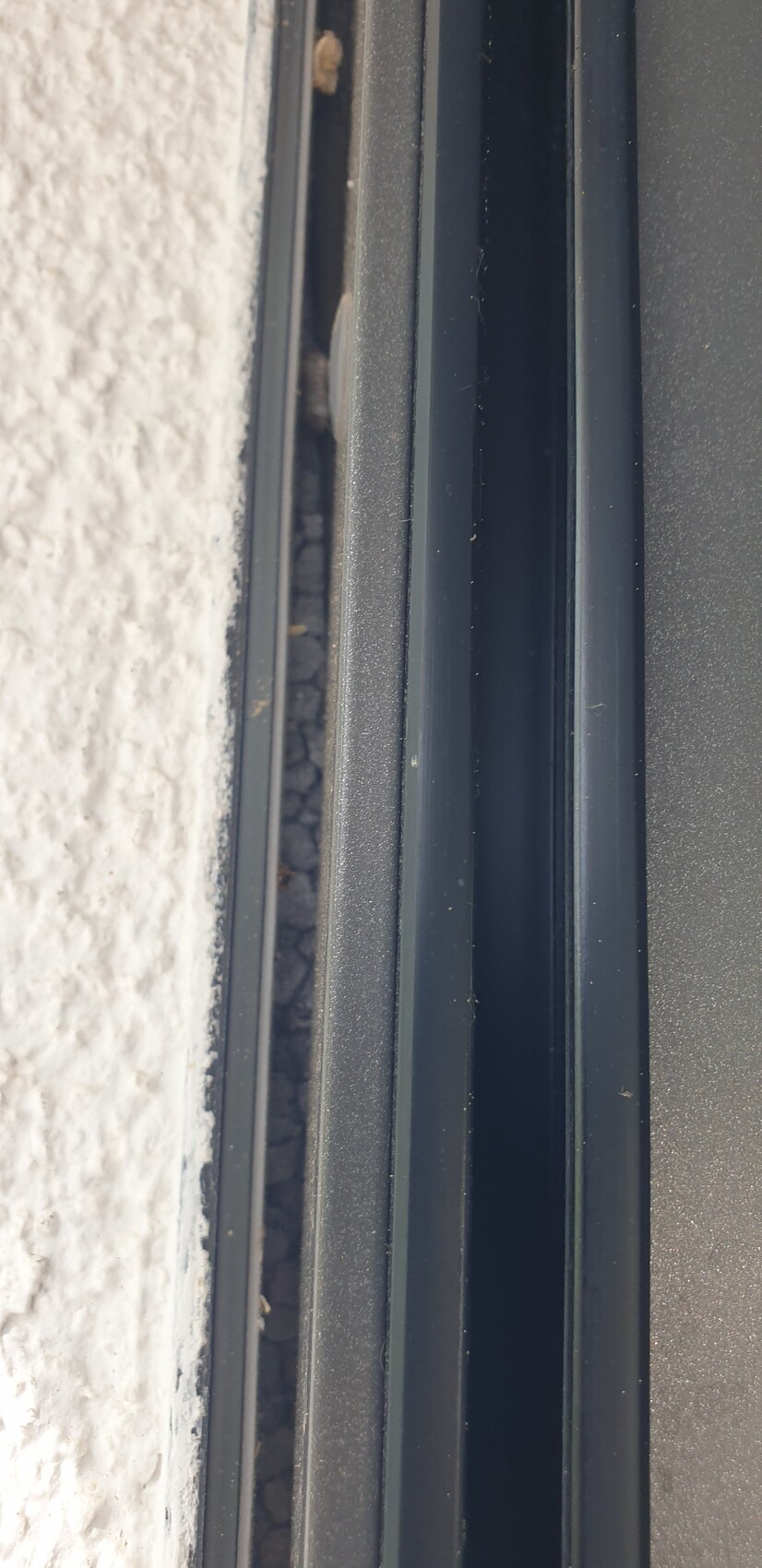Nahaufnahme eines Fensterrahmens mit Dichtung, Spalt zur weiß verputzten Wand sichtbar.