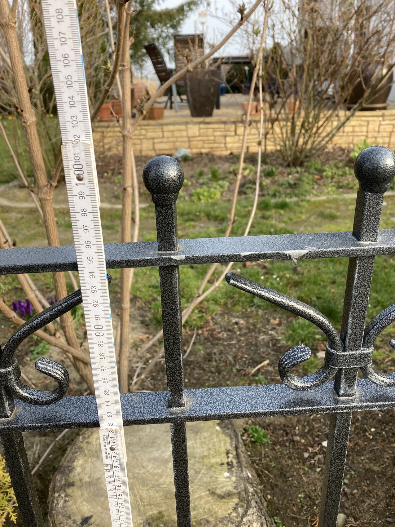 Schwarzer Metallzaun mit Kugelknauf, Messband zeigt Höhe ca. 1 m im Garten.
