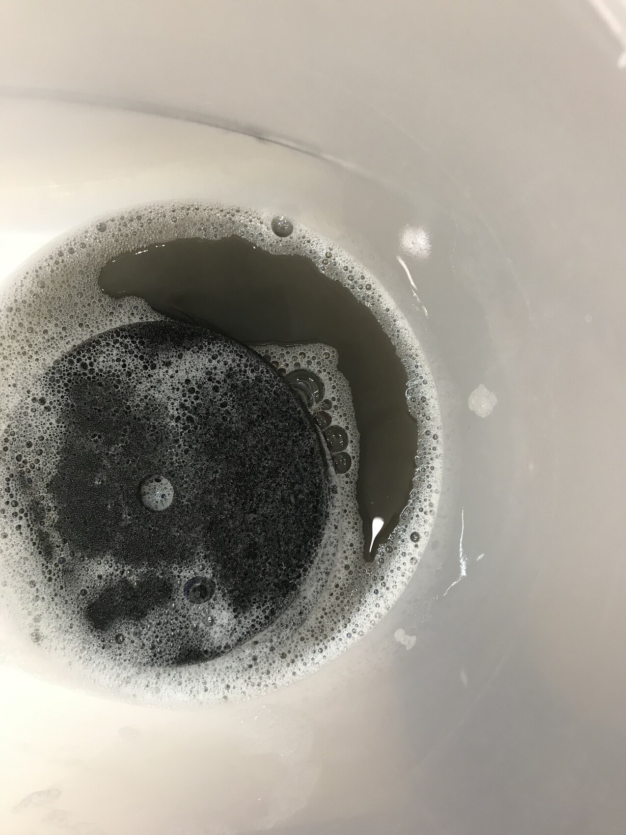 Waschbecken-Ablauf mit dunkler Flüssigkeit und Seifenblasen um den Abfluss.