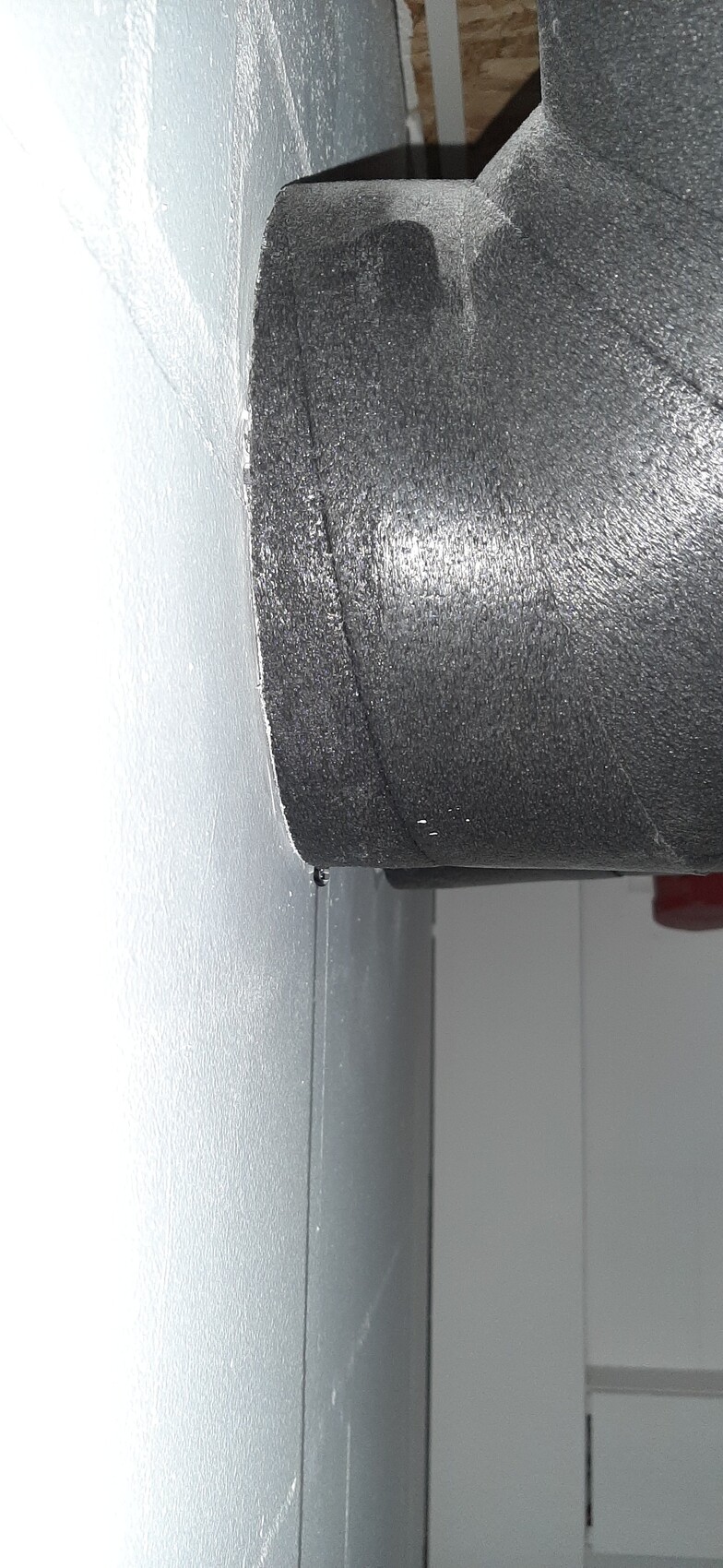 Große schwarze Walze aus grobem Material vor grauer Wand, Nahaufnahme eines Maschinenteils.