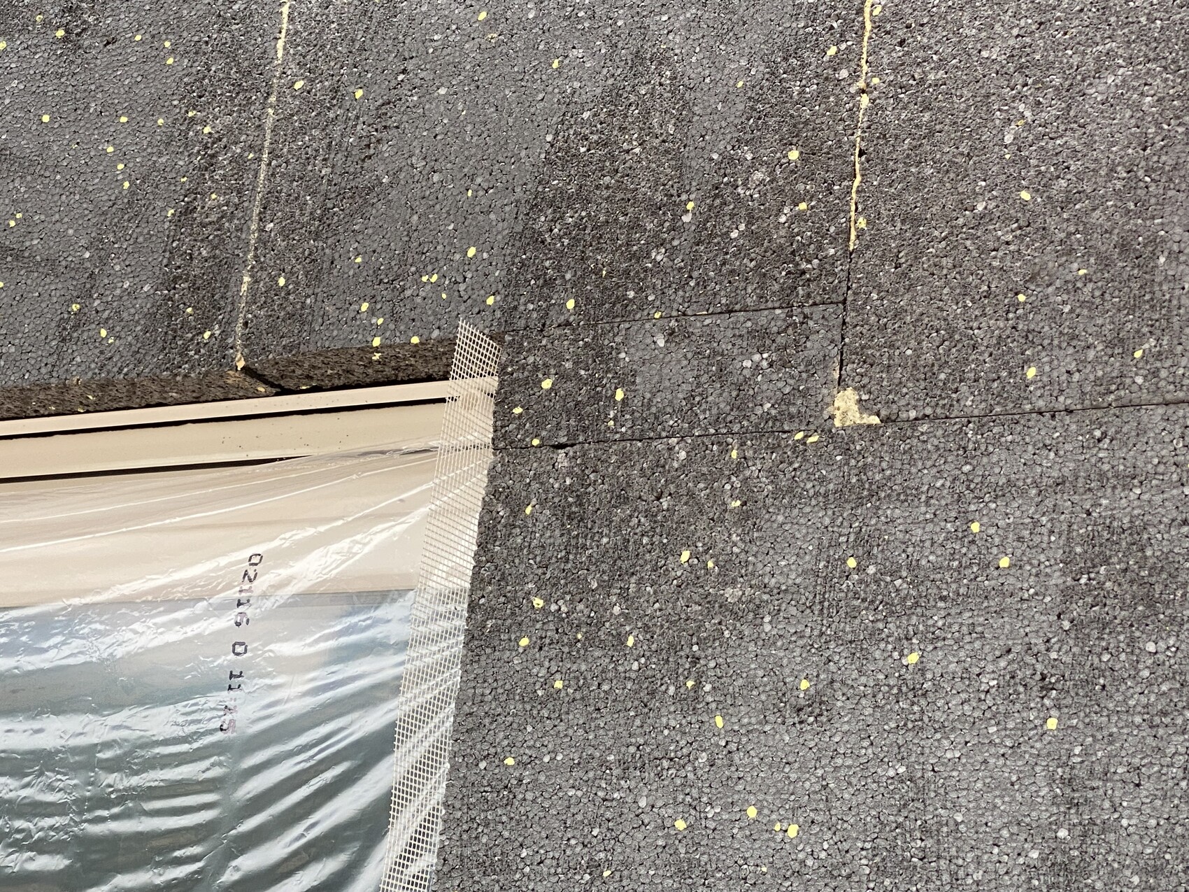 Dunkles Bitumen-Dach mit gelben Granulat-Flecken; Plastikfolie und Metallgitter liegen auf dem Dach.