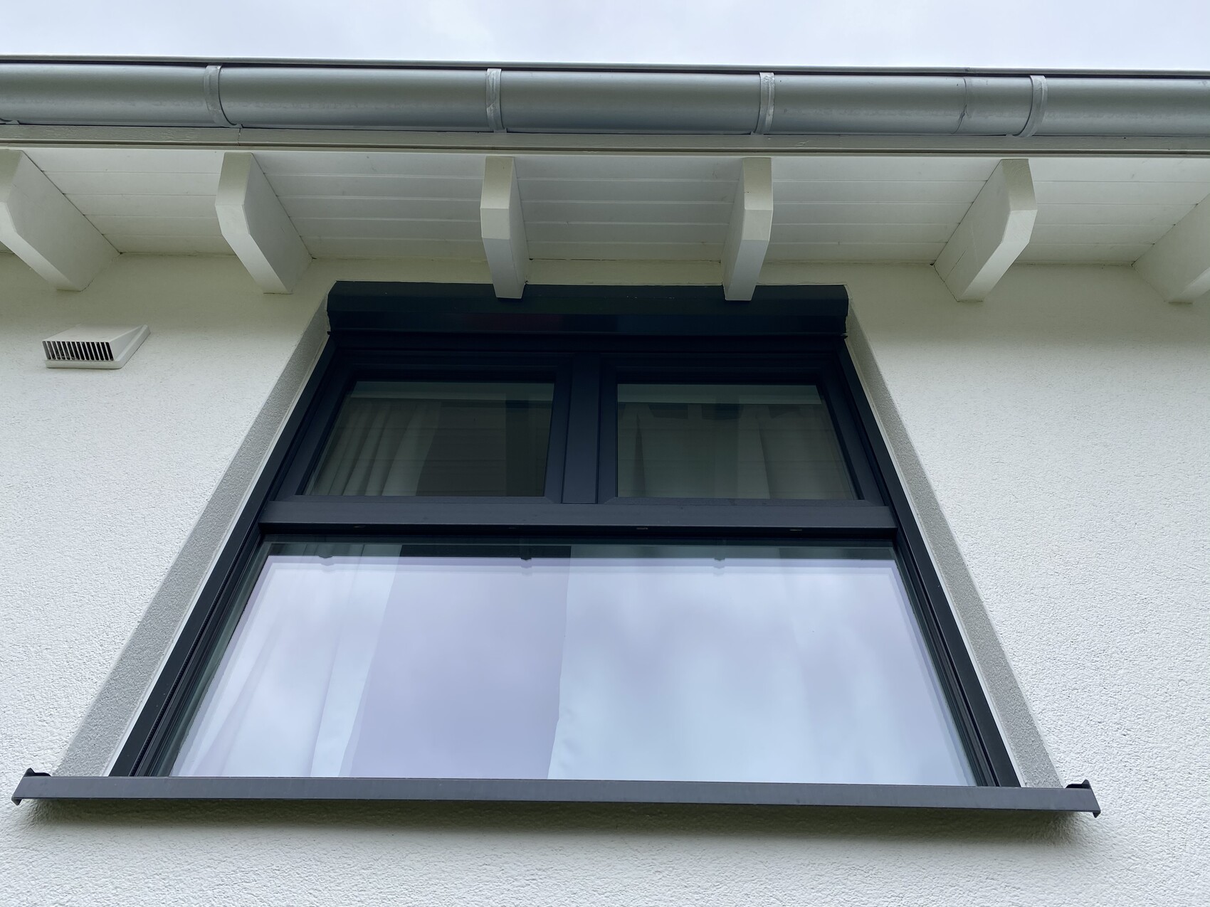 Außenansicht eines weißen Hauses mit schwarzem Fensterrahmen unter einem Dachüberstand.