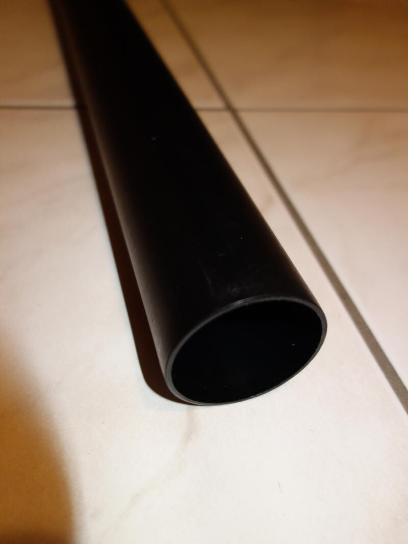 Nahaufnahme eines schwarzen PVC-Rohrs auf hellen Bodenfliesen, Sanitärinstallation