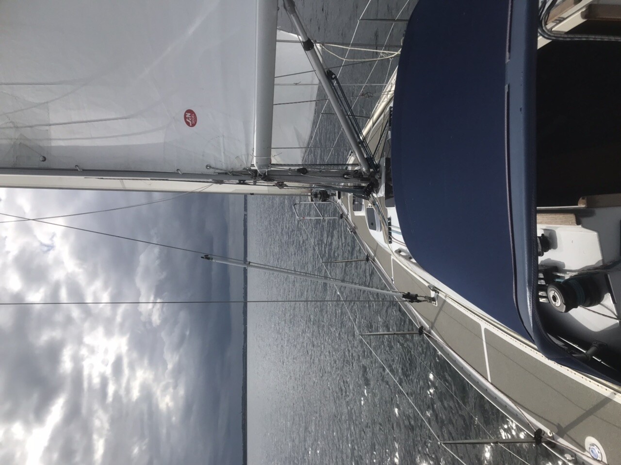 Segelboot auf dem Meer mit aufgebautem Großsegel, Mast und Takelage; blaue Sitzbank im Vordergrund