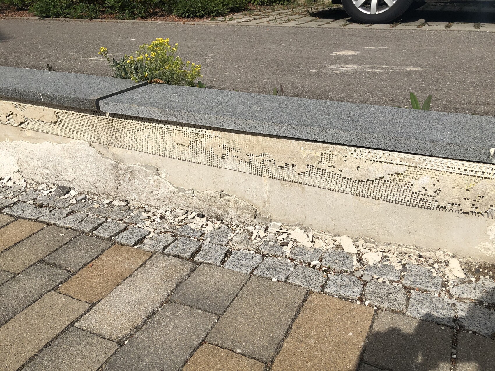 Beschädigte Betonmauer mit Steinverkleidung, Putz bröckelt, Pflastersteine am Gehweg