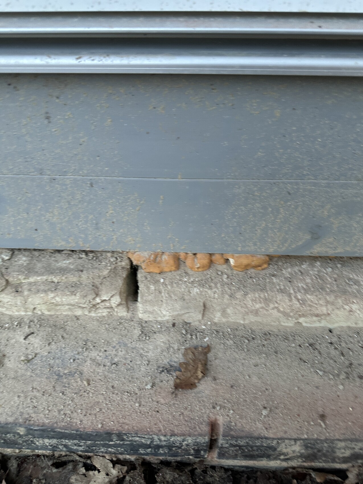 Grauer Metallrollladen über bröckelnder Betonstufe; am unteren Rand brauner Belag/Klumpen.
