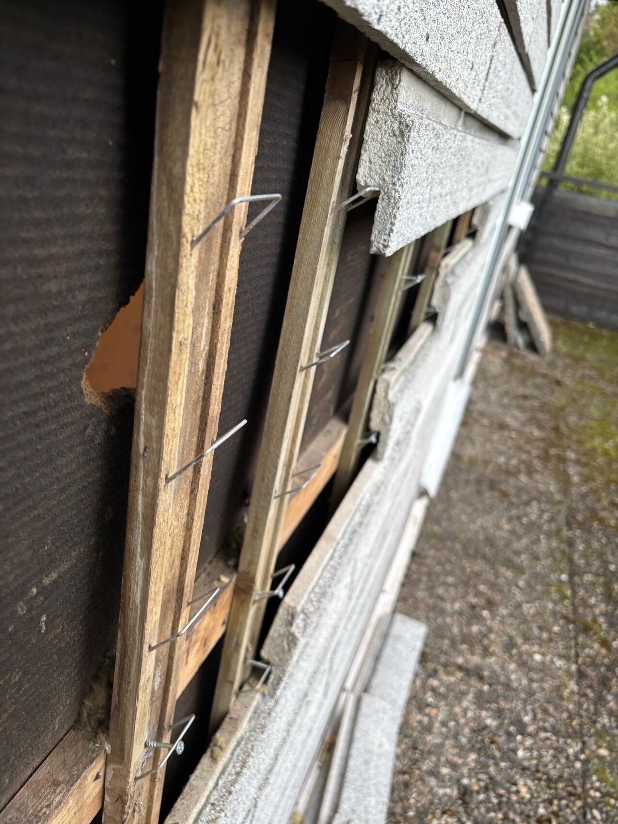 Außenwand eines Gebäudes mit freigelegtem Holzrahmen, Drahtstiften und Dämmplatten im Rohbau