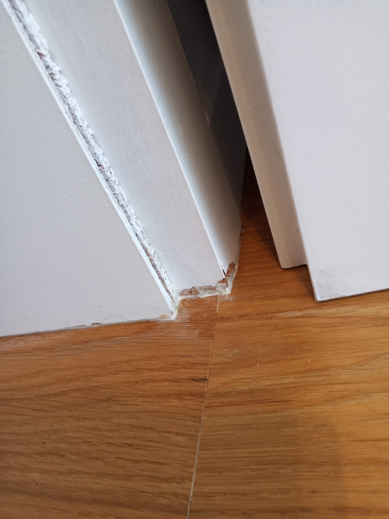Schadhafte Türzarge am Boden mit abblätternder weißer Farbe und freiliegendem Holzfußboden