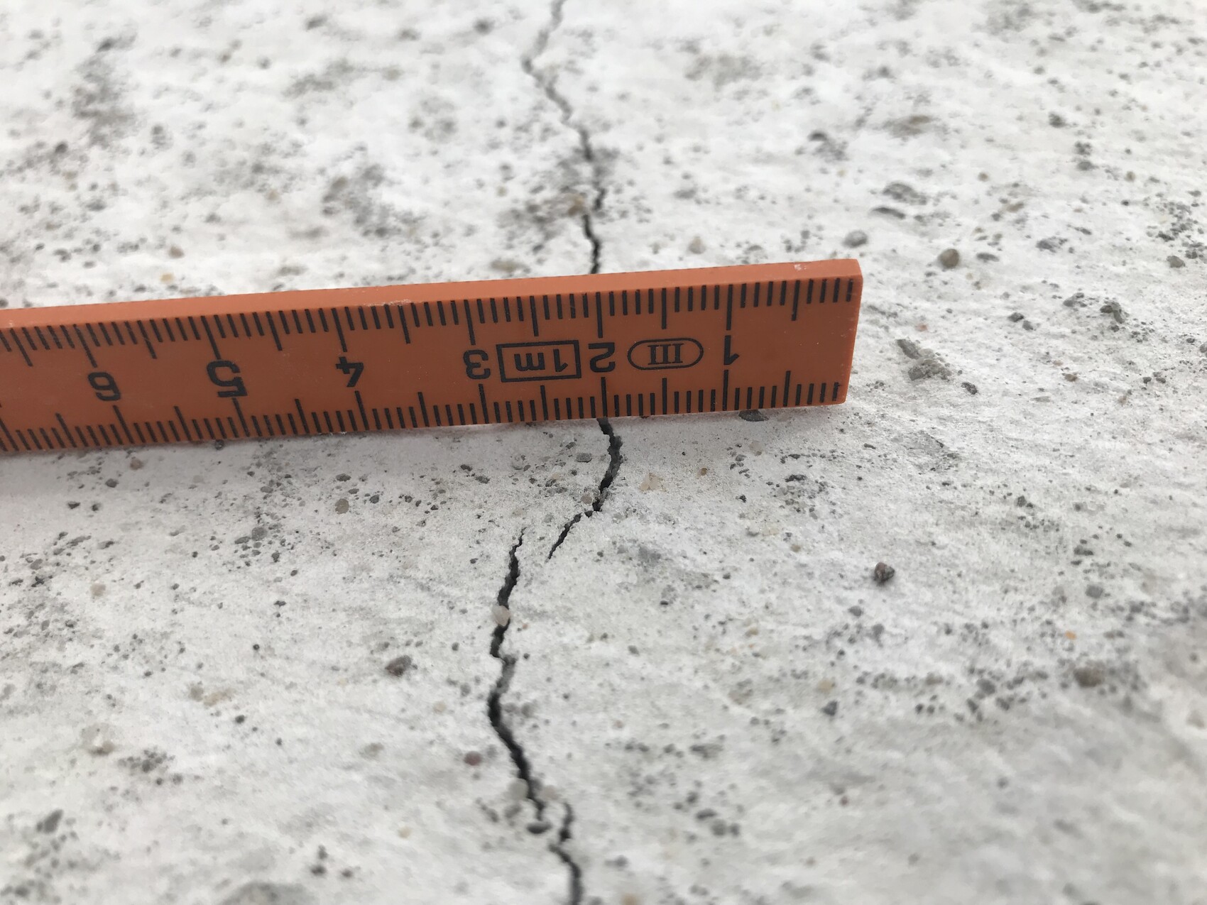 Nahaufnahme eines orangefarbenen Lineals auf Beton mit einem Riss