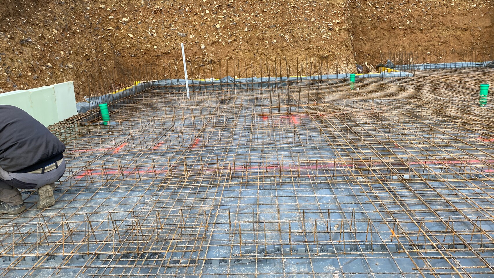 Bewehrungsstahlnetze liegen auf der Bauplatte; Arbeiter kniet beim Verlegen der Stahlstäbe.