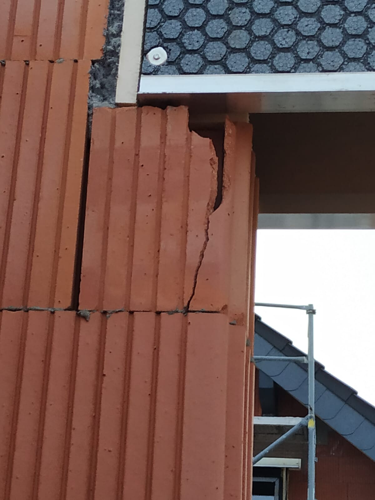 Rote Ziegelwand mit großem Riss an der Ecke, Baugerüst im Hintergrund.
