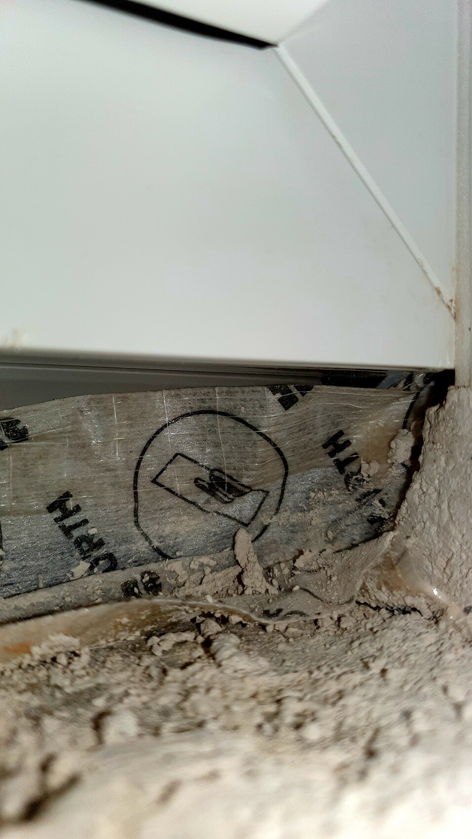 Weißes Metallgehäuse nahe einer Wand mit bröckelndem Putz und Dämmung, Staub sichtbar.