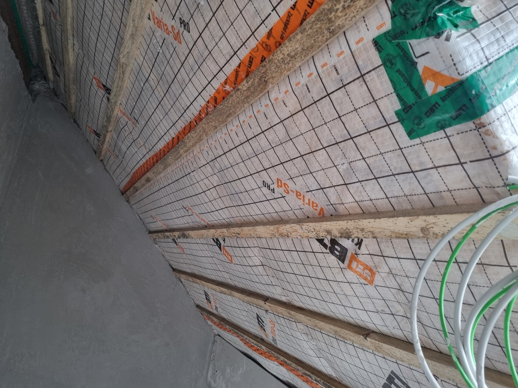 Innenansicht einer Baustellenwand mit Dämmfolie und Holzlatten; lose Kabel liegen bereit.