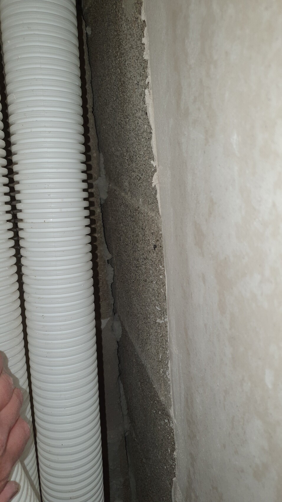 Zwei weiße, flexible Kabelrohre stehen an einer rauen Betonwand.