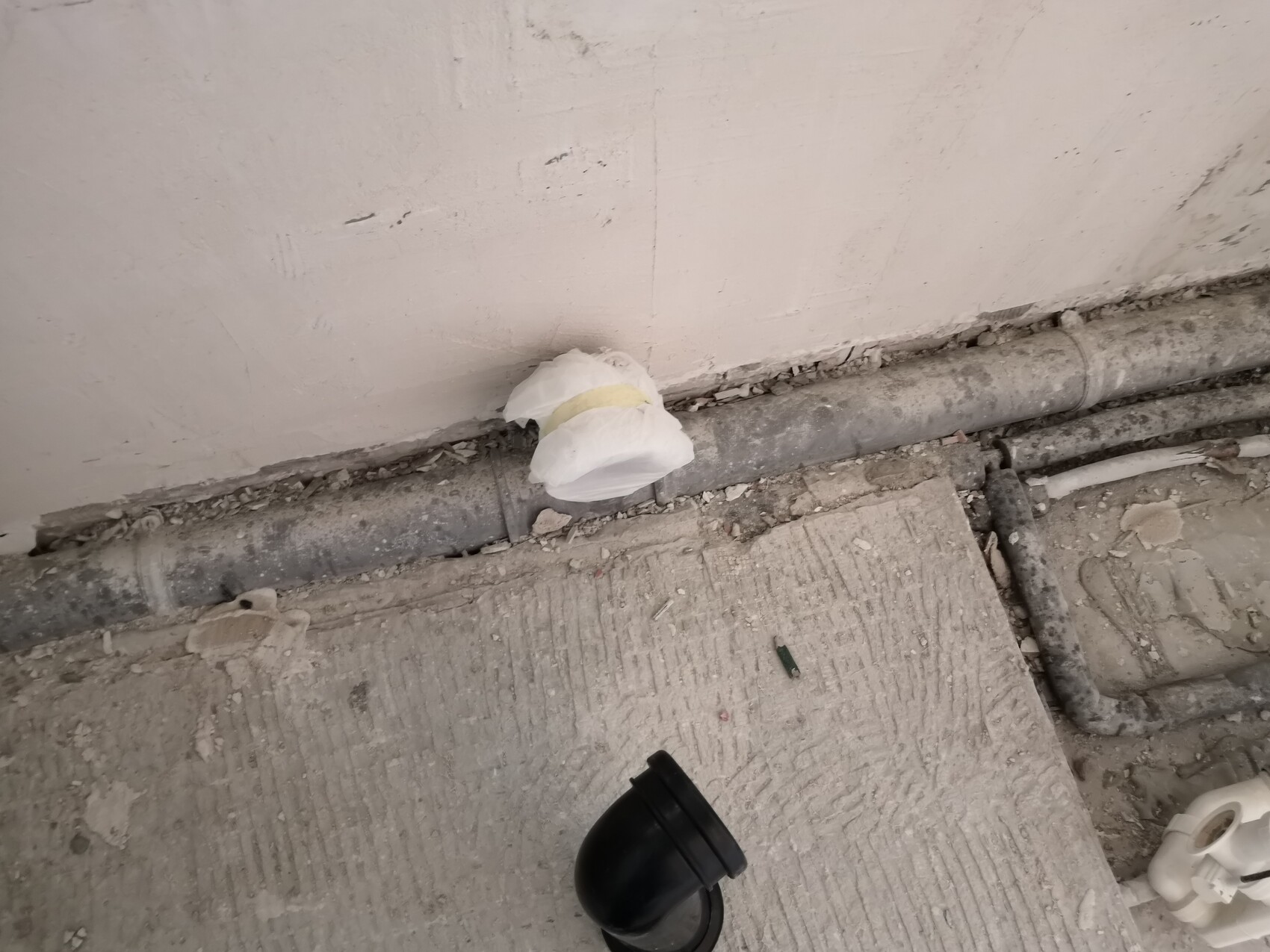 Weißer Sack mit gelbem Klebeband liegt auf einer Rohrleitung vor einer staubigen Baustellenwand.