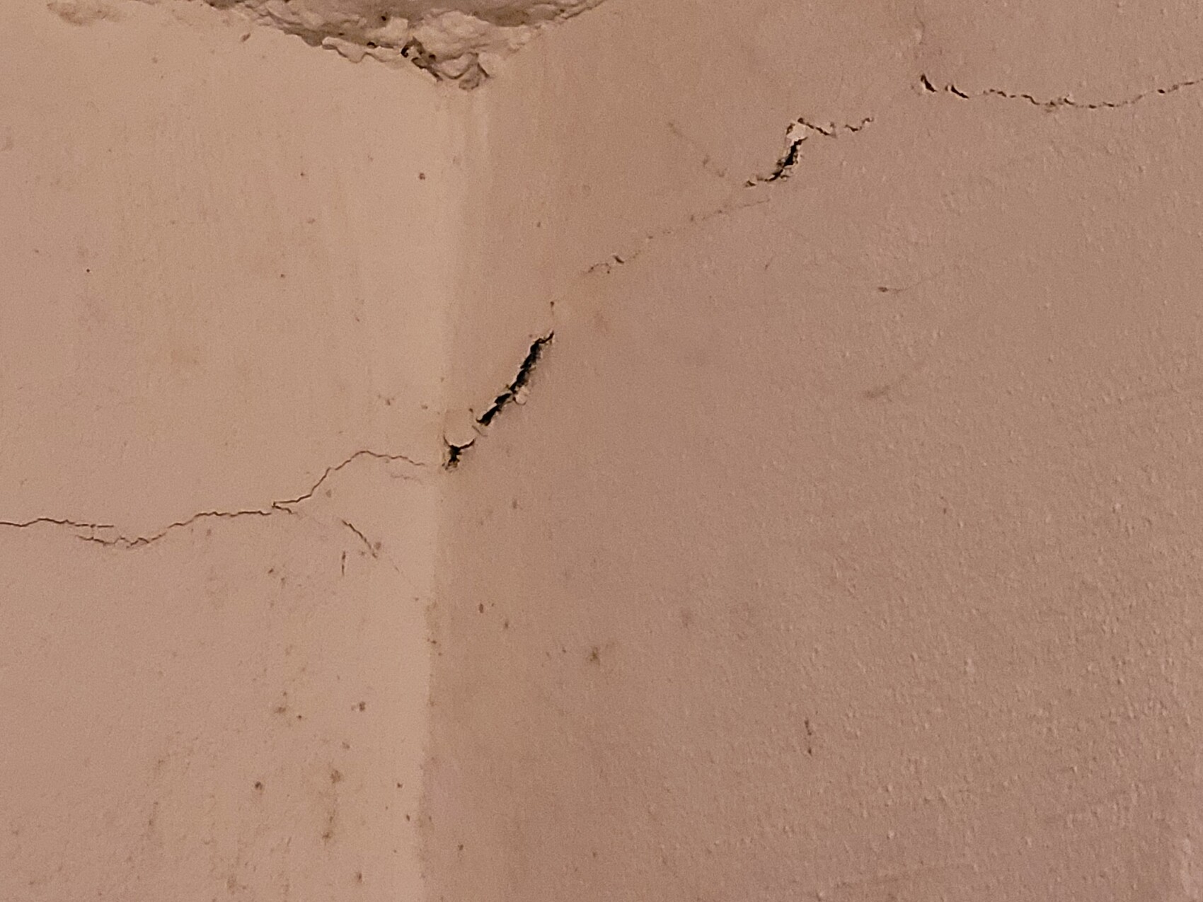 Nahaufnahme einer rissigen Putzwand mit feinen Rissen und dunklen Flecken, rosa Tönung