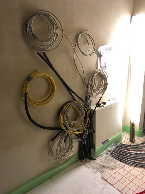 Mehrere Kabelrollen in Gelb, Weiß und Grau hängen an der Wand neben einem kleinen Verteilerkasten.