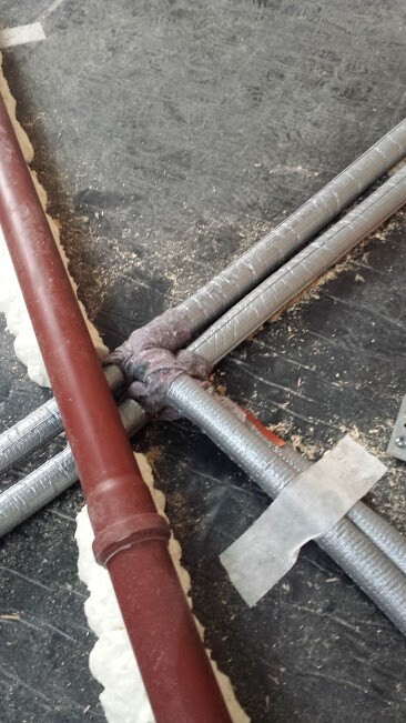 Kreuzweise liegende Metallrohre und ein rotes Rohr liegen auf einer Baustellenfläche.