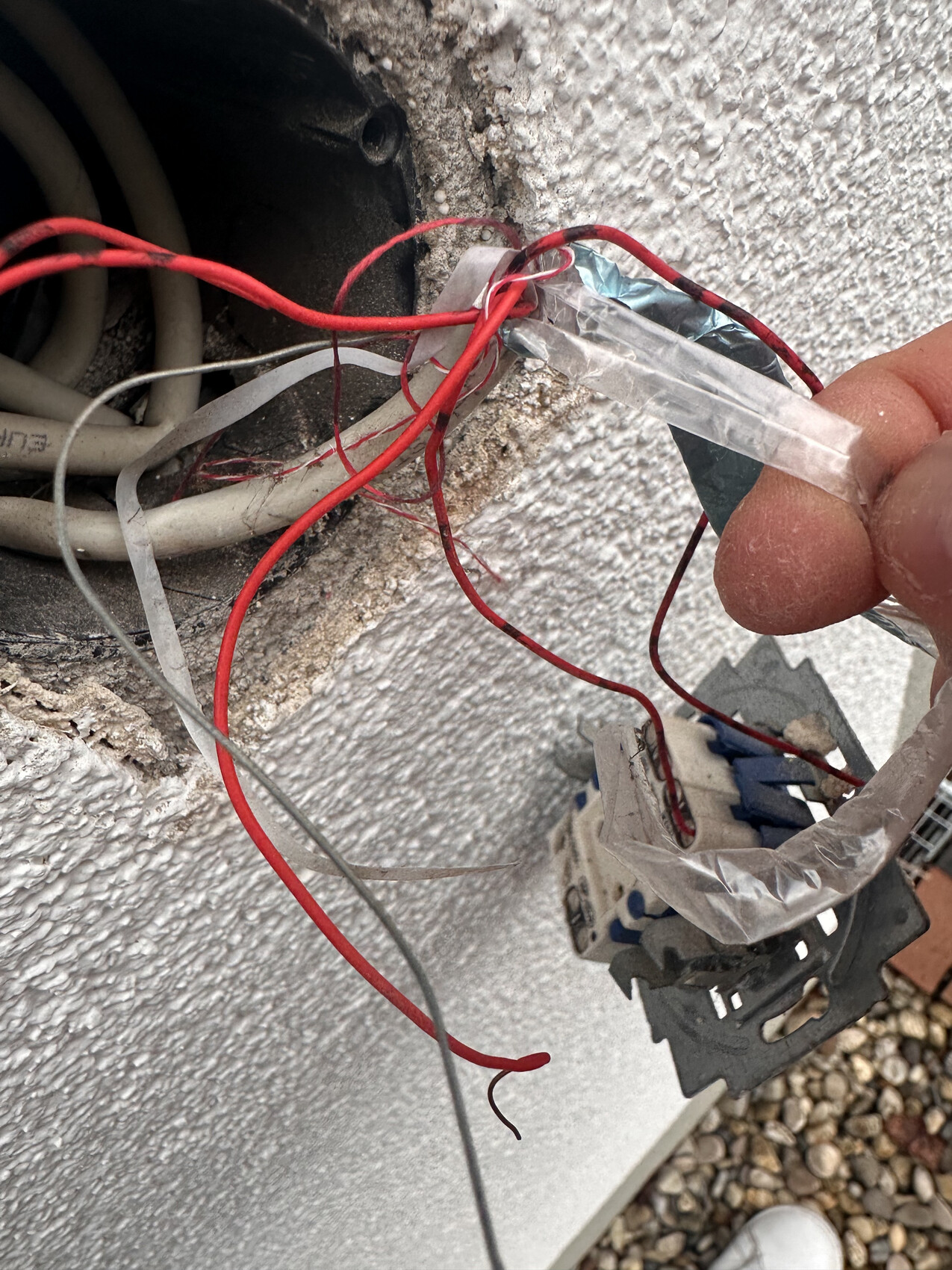 Außenwand: offene Elektroverkabelung mit roten Drähten, Isolierband und Schalterteil.