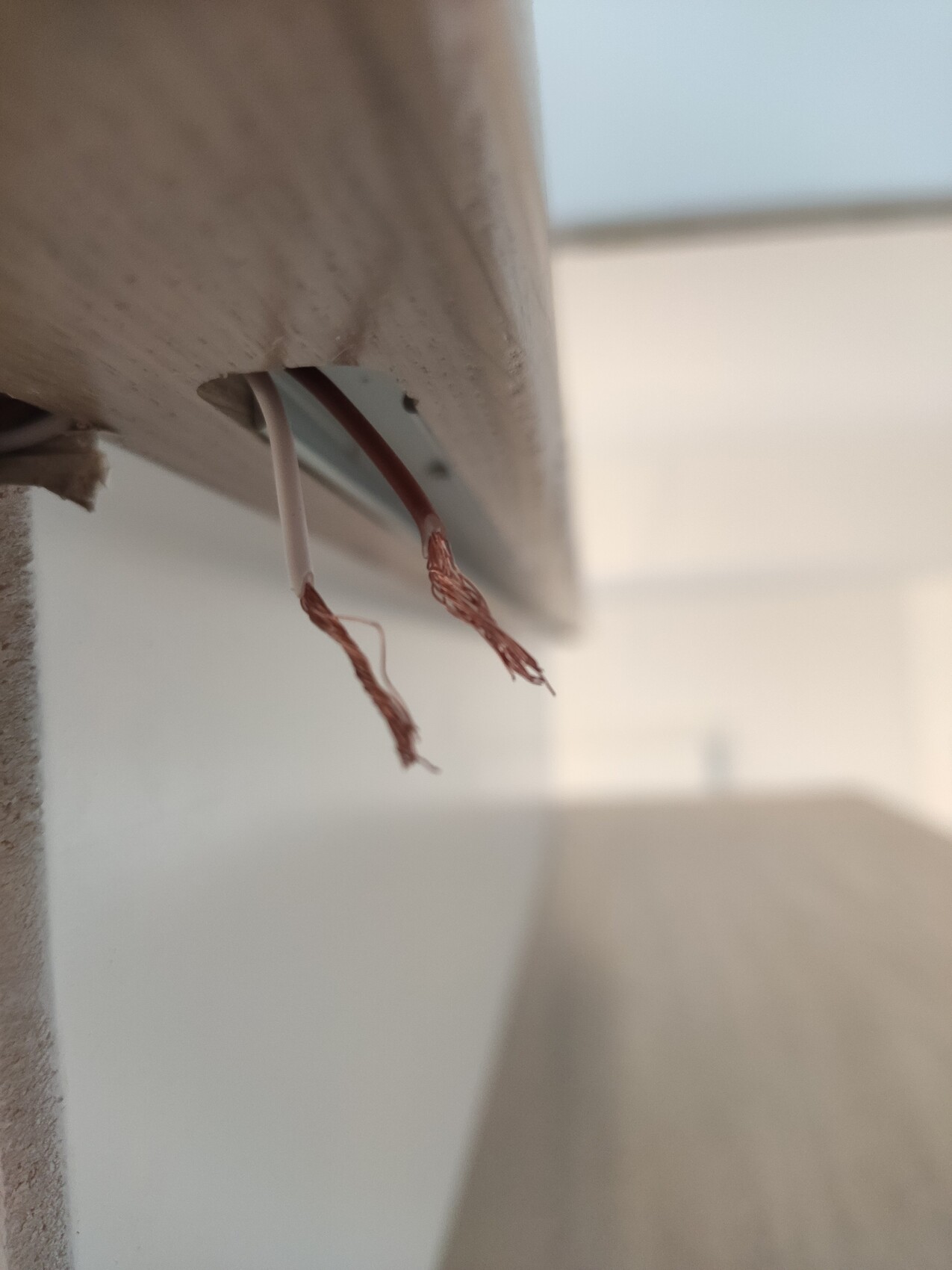 Unter einer Holzverkleidung freiliegende Kupferlitzen aus Kabeln.