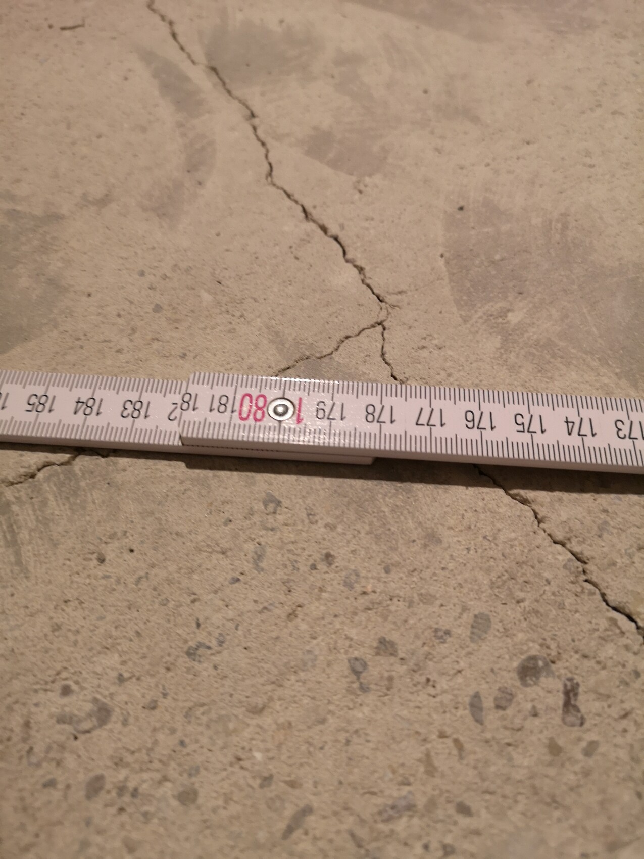 Betonboden mit sichtbarem Riss und Messband.