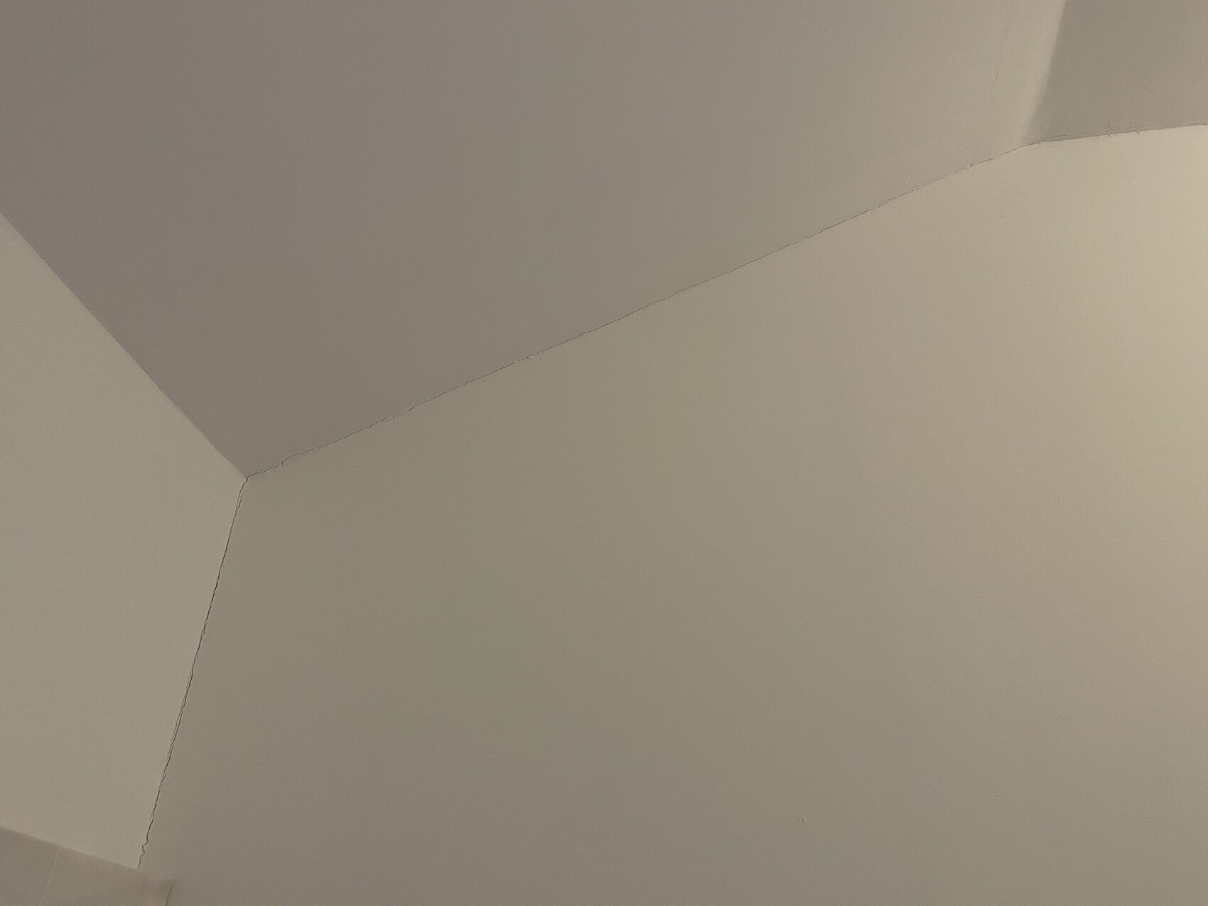 Nahaufnahme einer Decken-Wand-Ecke mit sichtbarer Risskante in beigefarbener Oberfläche.